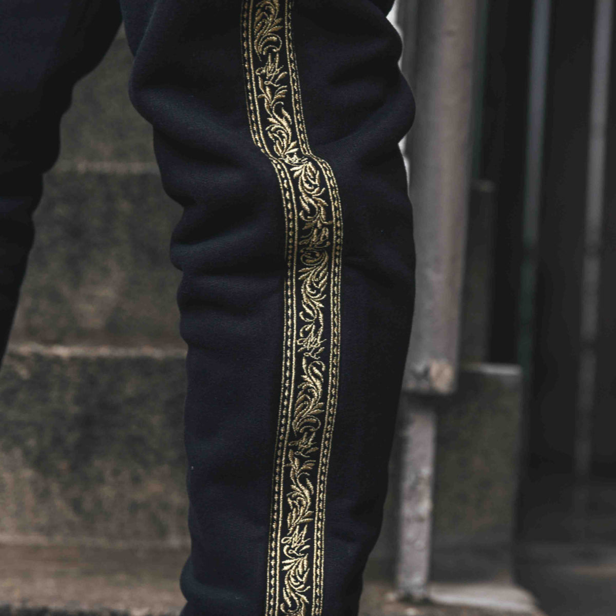 Gros plan de la bande brodée Meander dorée le long de la jambe du pantalon de jogging MVL noir