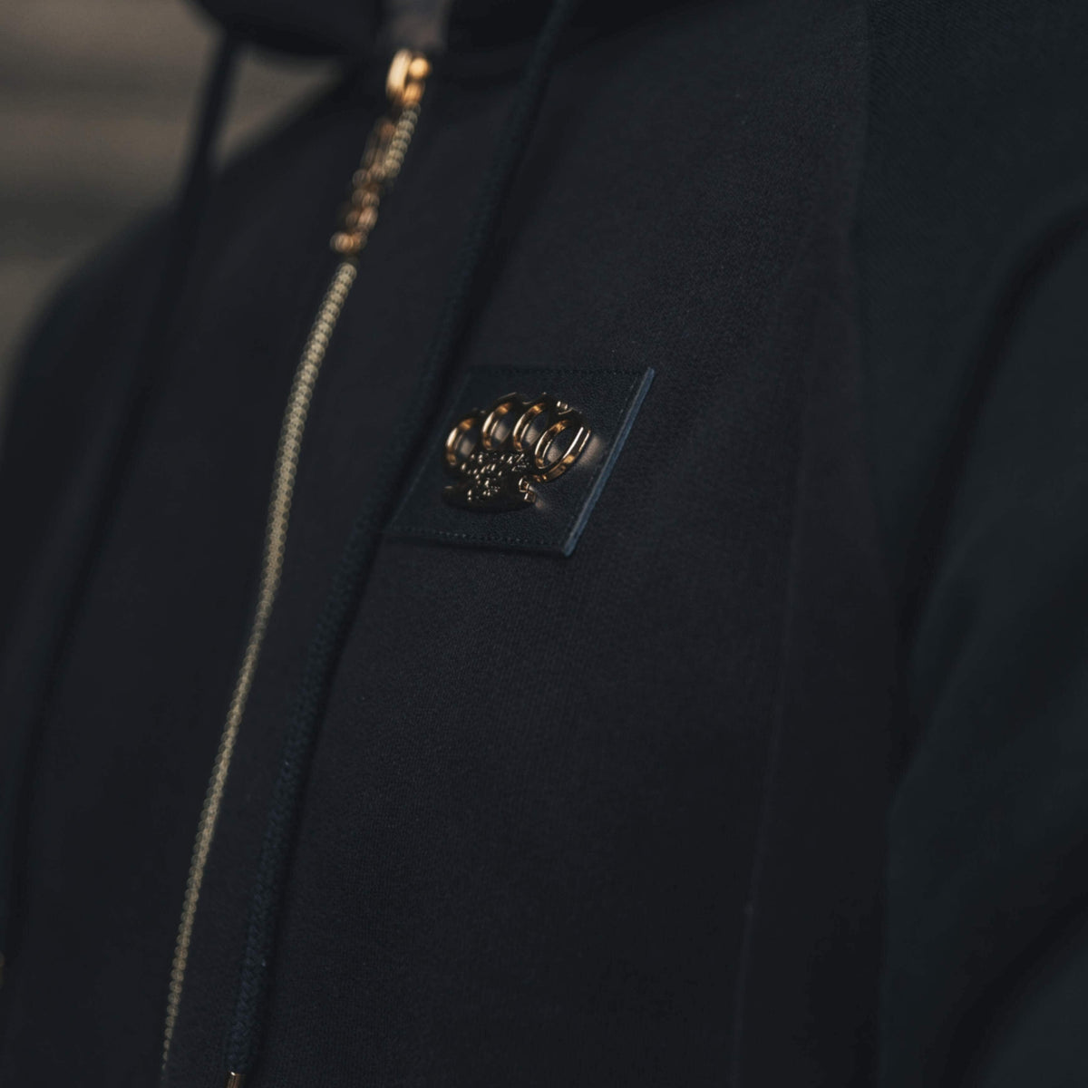 Gros plan du logo MVL doré sur la poitrine et de la fermeture éclair du hoodie Meander noir