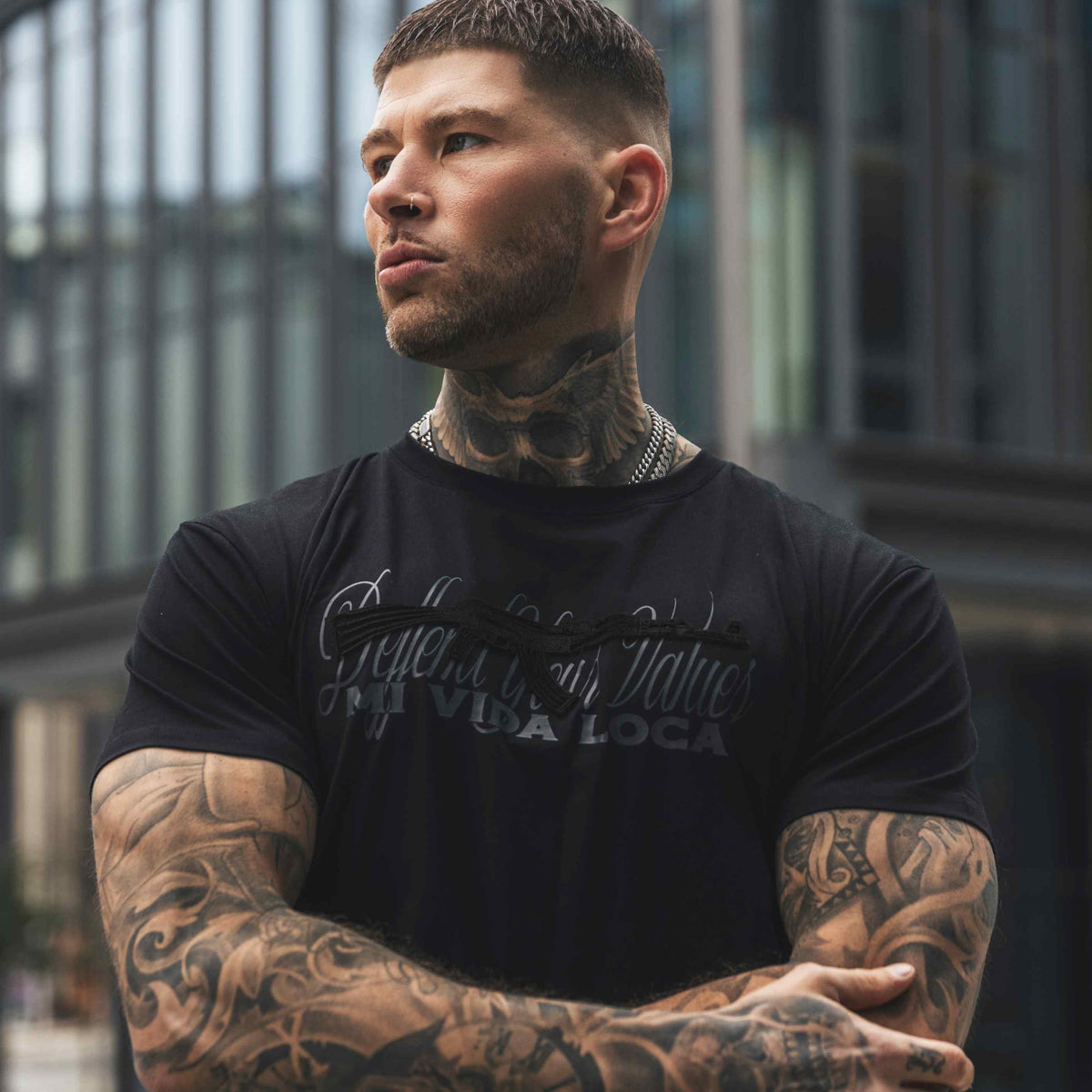 Modelo con los brazos cruzados con la camiseta MVL Defend your values negra, vista frontal