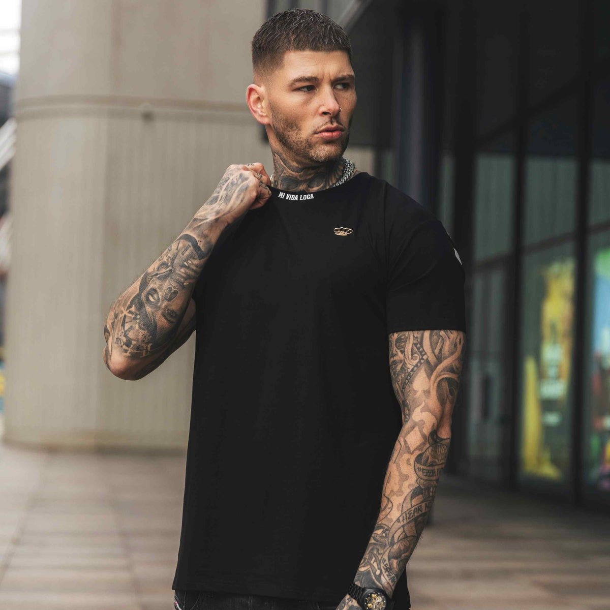 Model trägt das schwarze MVL FTS T-Shirt, Vorderseite mit kleinem Logo, in einer Stadtstraße