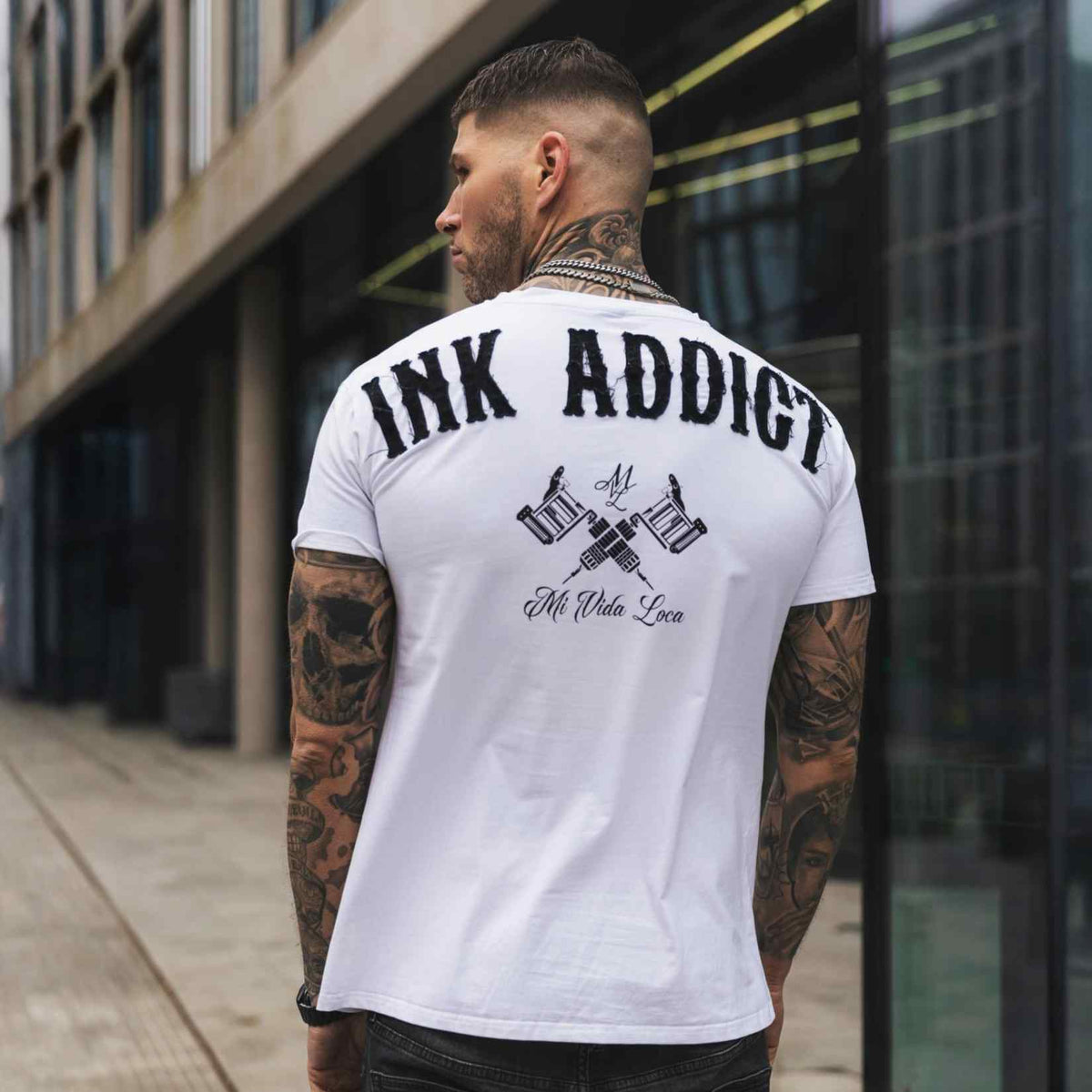 Tył białej koszulki Ink addict z nadrukiem na plecach, na wytatuowanym modelu w mieście