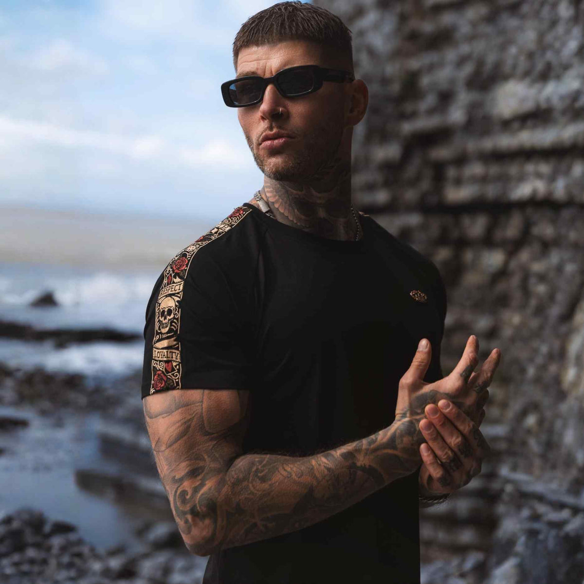 Model in sunglasses in the black LFR T-shirt with colourful sleeve band on the coast
