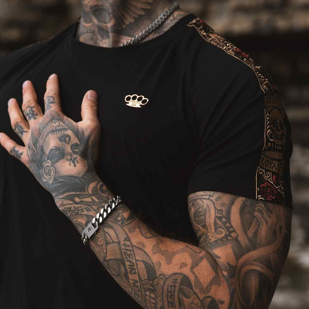 Close-up of the gold MVL logo on the chest and the LFR sleeve band of the black T-shirt, worn