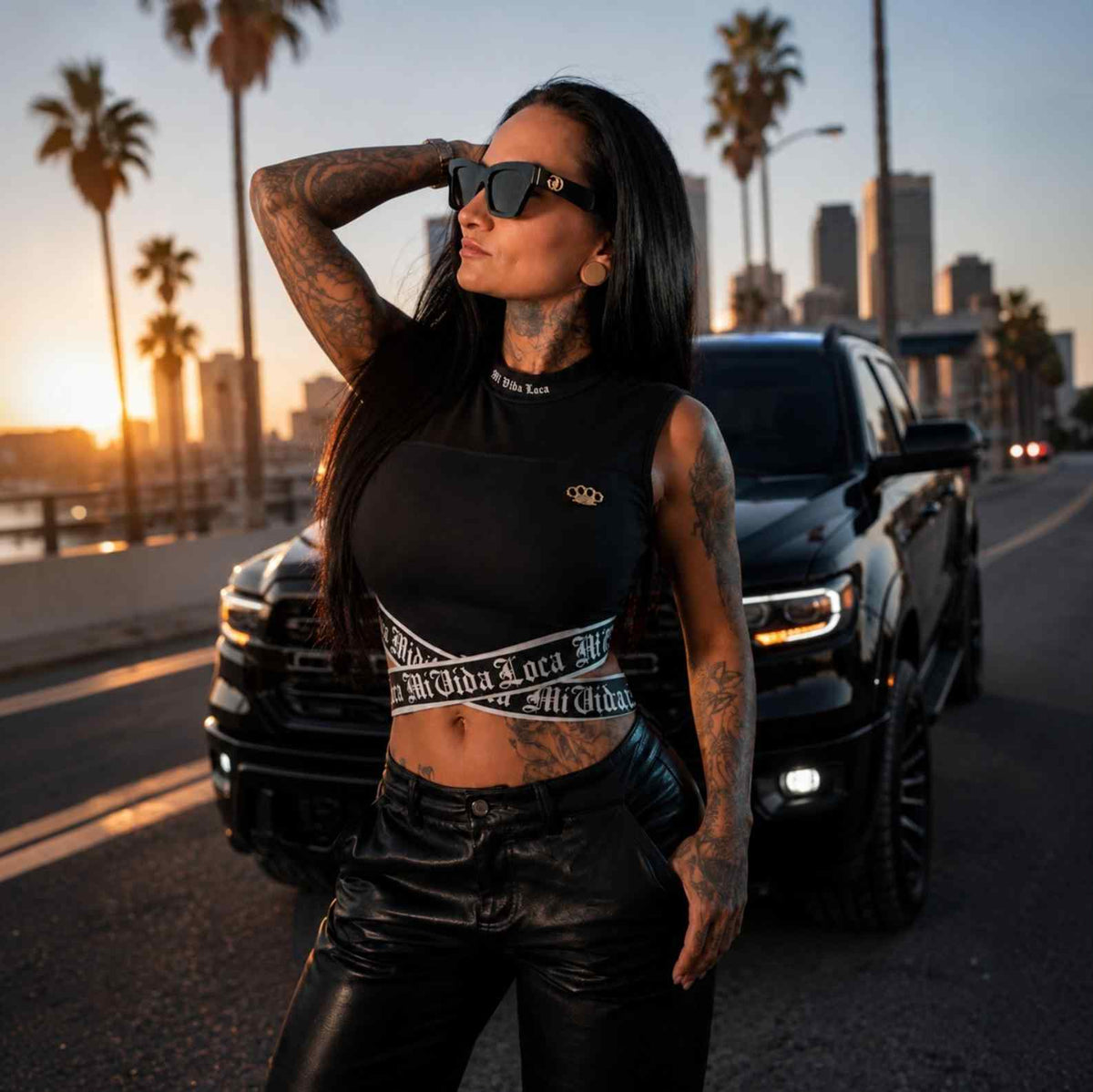 Signature Damen-Top schwarz, getragen von Model mit Sonnenbrille bei Sonnenuntergang zwischen Palmen